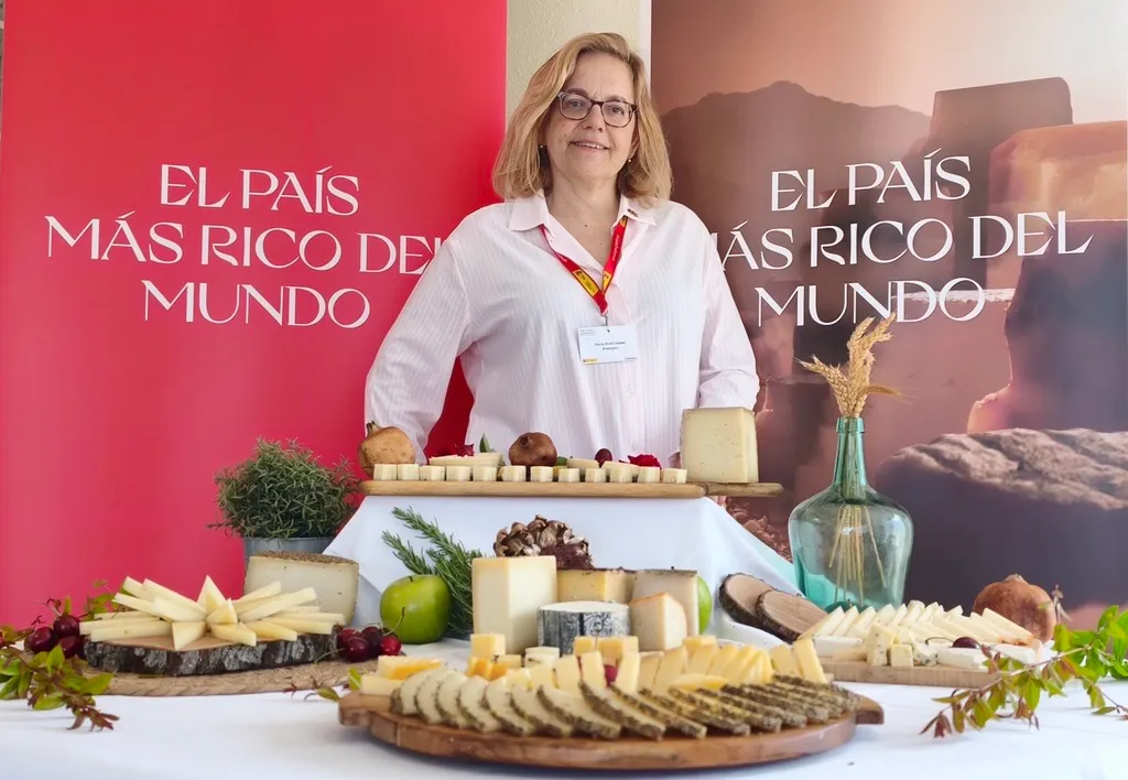 Ruth Lozano de pie tras una mesa con una gran selección de quesos españoles cortados en cuñas y tacos, en un evento de promoción agroalimentaria.
